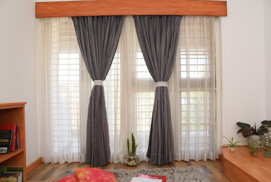 Charcoal semi-blackout curtains tied back over sheers, under a wooden pelmet